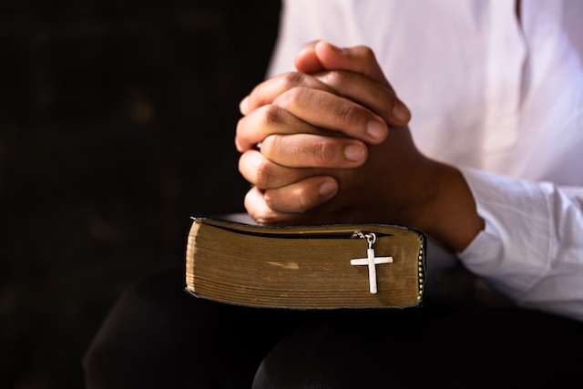 Hands folded in prayer on a Holy Bible in church concept for faith
